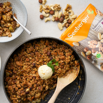 Eine Schüssel mit knusprigem Crumble, serviert mit Vanilleeis, daneben liegt eine Nusspackung.