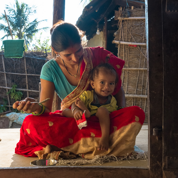 Frau hat Kind auf dem Schoß und füttert ihn mit Brei