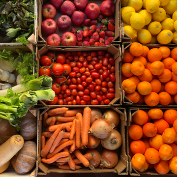 Kisten voller farbiger Früchte und Gemüse stapeln sich auf einem Marktstand.