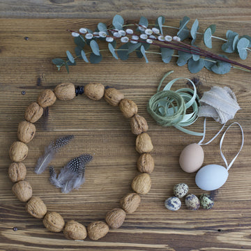 Walnusskranz liegt auf Holztisch, umgeben von Eukalyptus, Federn, Eiern und Bändern.