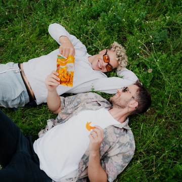 Zwei Personen liegen auf Wiese, essen „Seeberger“-Snack, und tragen Sonnenbrillen, sommerliche Atmosphäre.