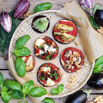 Auberginenscheiben mit Belägen ruhen auf einem Korb, umgeben von frischem Basilikum.