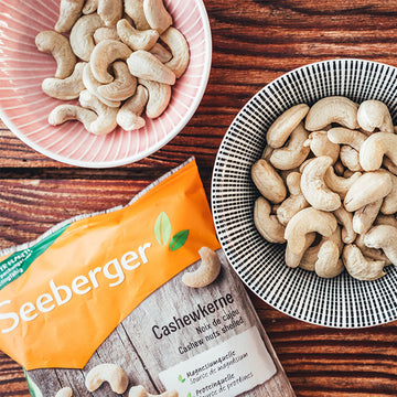 Schalen mit Cashewkernen stehen auf Holztisch, daneben eine Seeberger-Verpackung.