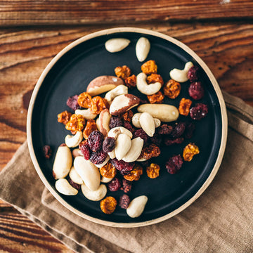 Ein Teller mit Nüssen und Trockenfrüchten liegt auf einem hölzernen Tisch.