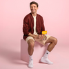 Thomas Müller sitzt lächelnd auf einem pastellpinken Würfel vor einem pastellpinken Hintergrund mit einem Seeberger Produkt in der Hand.