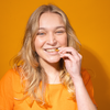 Eine lächelnde Frau isst Chips vor einem orangefarbenen Hintergrund.