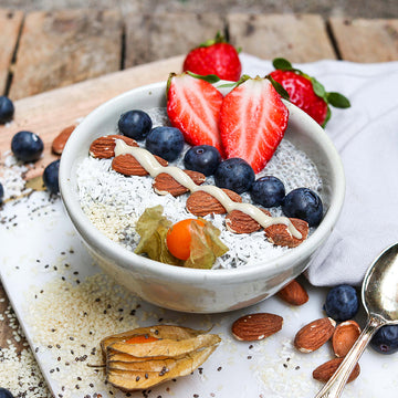 Schale: Enthält Chia-Pudding, Beeren, Mandeln; dekoriert auf Holztisch mit verstreutem Obst.
